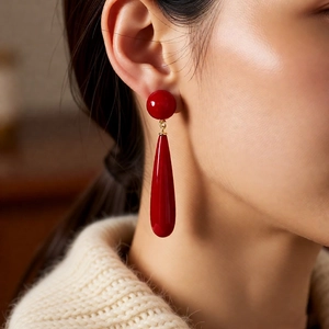 Close-up of bright red drop earrings with round studs on a model in a cozy knit sweater