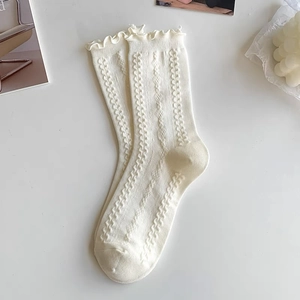 Detail of cream calf-high socks featuring ruffle cuffs and geometric knit texture