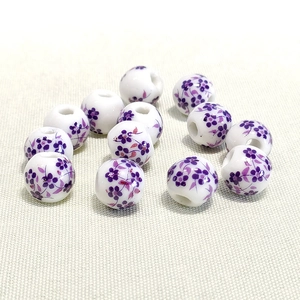 Macro shot of 10mm white ceramic beads with purple floral patterns and threading holes
