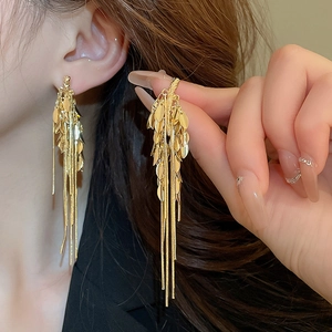 Detailed view of long gold tassel earrings with leaf motifs and snake chain fringes