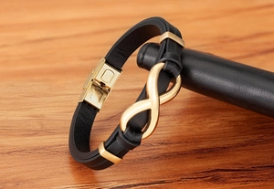 Detail of black leather bracelet with golden infinity charm and stainless steel magnetic clasp