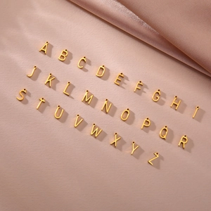 Golden 18K stainless steel A-Z alphabet charms displayed on pink silk background