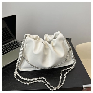 Close-up of white pleated leather cloud bag with silver chain strap on a desk