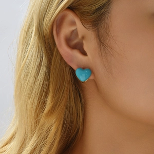 Close-up of a blue enamel heart-shaped earring worn on a model's ear with golden edges