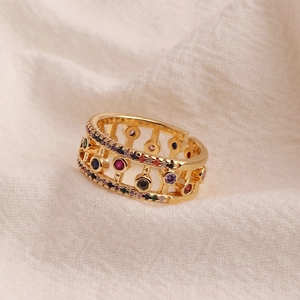 Detail of gold hollow ring with colorful zircon stones on textured white fabric