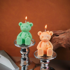 Close-up of green and orange cartoon bear candles with bowties on a silver holder