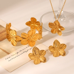 Artistic flat lay of 18K gold textured flower necklace, bracelet and earrings set