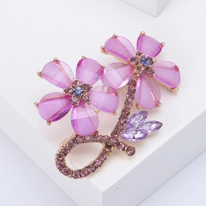 Elegant gold flower brooch with pink crystals and purple rhinestones on white pedestal