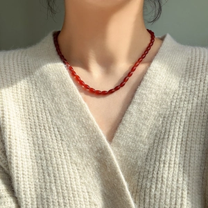 Detail of red agate beaded necklace with smooth barrel beads worn on a cream sweater