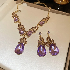 Close-up of luxury gold-tone jewelry set with purple teardrop crystals in a gift box
