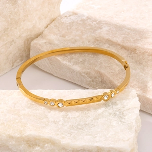 Gold stainless steel bangle featuring wave patterns and diamond accents on stone background