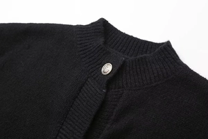 Detail eines strukturierten silbernen Metallknopfs an einer schwarzen Strickjacke