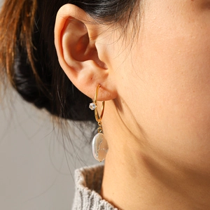 Gros plan sur boucle d'oreille dorée avec perle baroque et pierre de zircon brillante