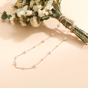 Detail of elegant gold chain necklace with alternating white pearls on warm beige background