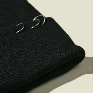 Détail du bonnet en maille noire avec anneaux métalliques argentés sur le bord replié