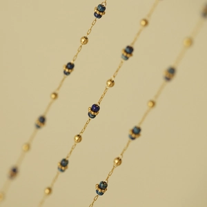 Dettaglio della collana a catena dorata a strati con perle blu e piccoli distanziatori dorati