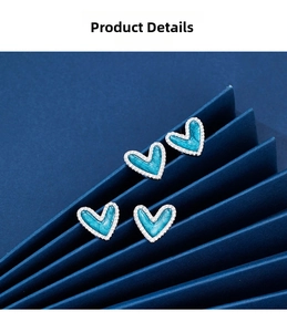 Macro view of blue enamel heart earrings with shimmering zircon edges on blue backdrop