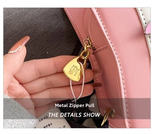 Detailed close-up of golden shield-shaped metal zipper on pink and white leather guitar bag