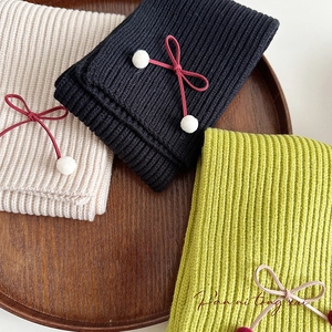 Detailed view of beige black and green knitted scarves with decorative bow and pom poms