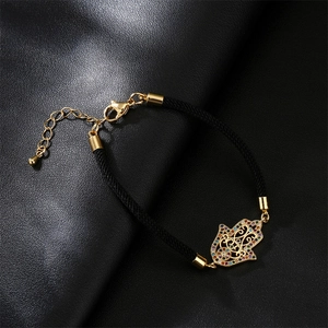 Detailed close-up of a Hamsa hand charm with colorful zircons on a black woven bracelet
