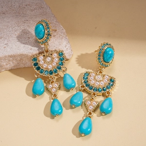 Close-up of ethnic drop earrings with turquoise stones, pearls, and crystals in gold setting