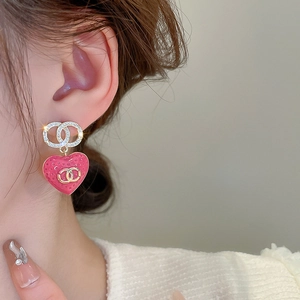 Close-up of pink heart earrings with gold emblem and shimmering crystals on model