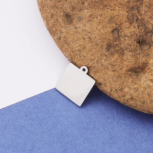 Polished square stainless steel charm tag for DIY jewelry displayed on a natural rock