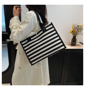 Fashionable black and white striped canvas tote bag worn by model in a modern home setting