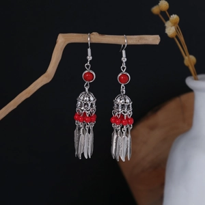 Detailed close-up of Bohemian silver feather tassel earrings with red beads on wood