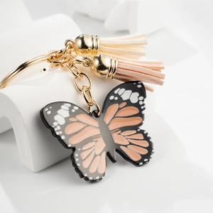 Detail of butterfly keychain with colorful tassels and gold metal clips on white blocks