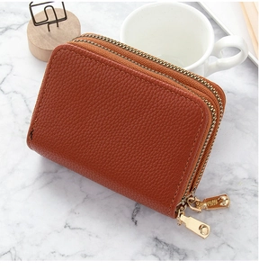 Detalle de cartera marrón con textura de lichi y cremalleras metálicas doradas dobles