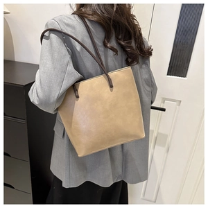 Minimalist beige bucket bag with thin shoulder strap shown in use by a model