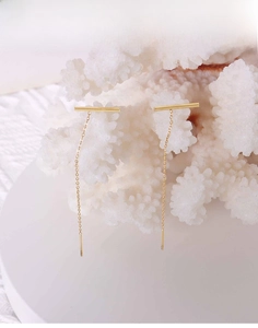 Detailed view of minimalist 18k gold linear drop earrings displayed on white decor