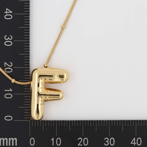 Macro shot showing dimensions of the gold puffy letter F balloon pendant necklace