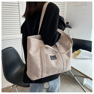 Close-up of stylish beige canvas tote bag worn by a model in a minimalist office setting