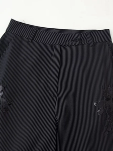 Détail d'un pantalon rayé avec une broderie de paillettes noires et des boutons en résine