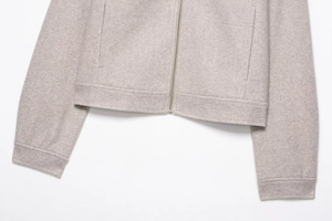 Detail view of smooth metal zipper and textured wool fabric on beige bomber jacket