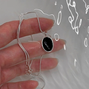 Minimalist S925 silver necklace with black oval agate pendant held in rippling water