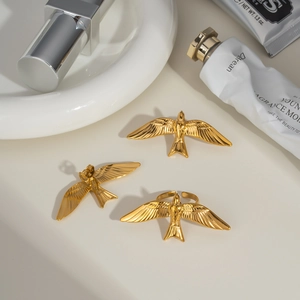 Détail macro de trois bijoux dorés en forme d'hirondelle stylisés avec des cosmétiques