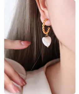 Close-up of elegant gold twisted hoop earring with white heart pearl pendant on model