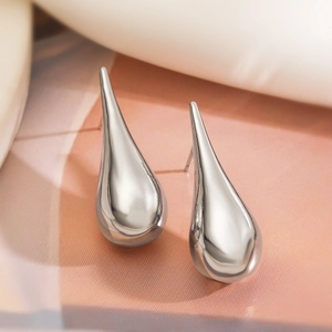 Macro shot of silver teardrop earrings on soft fabric showing sleek metallic texture