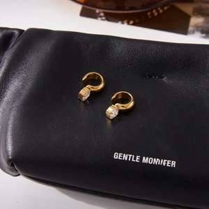 Close-up of golden stainless steel hoop earrings with round zircon on black leather pouch