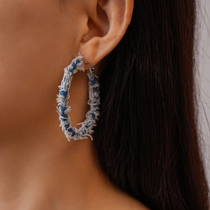 Detail view of denim geometric hoop earrings with distressed fringe on a model
