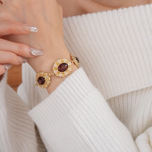 Close-up of vintage gold bracelet with deep red oval gemstone and white flower accents