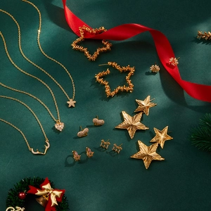 Dettaglio del set di gioielli placcati oro con stelle e cuori su sfondo natalizio rosso