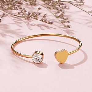 Dettaglio del bracciale aperto a cuore dorato con cristallo su sfondo rosa con fiori