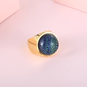 Exaggerated gold stainless steel ring with deep blue star-glass orb on pink background