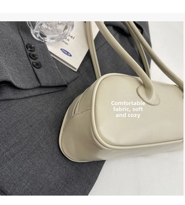Detail view of a cream baguette shoulder bag on a grey blazer with slim straps