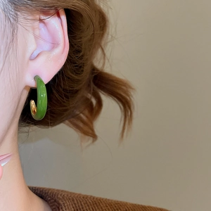 Macro side view of a model wearing green enamel C-shaped earrings with gold metal lining
