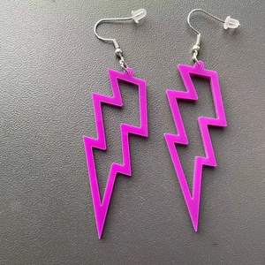 Detail view of pink acrylic lightning bolt earrings with metal hooks on grey background